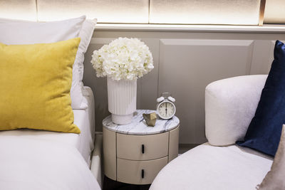 Alarm clock showing 6 o'clock on a bedside table and white flower.