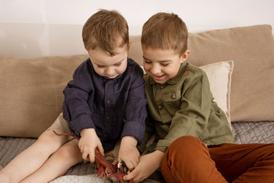 Two little and cute caucasian boys playing with dinosaurs at home. 