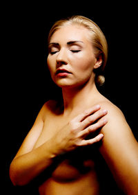 Topless young woman covering breasts against black background