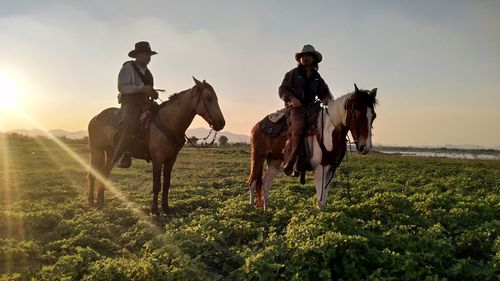 Men riding horses on field against sky