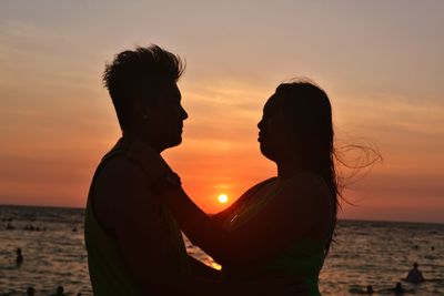 Silhouette couple embracing by sea against sky during sunset