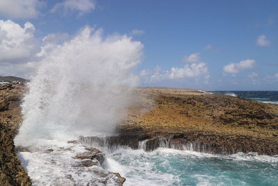 Waves splashing on rocks against sky