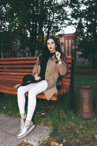 Portrait of beautiful woman sitting on bench at public park