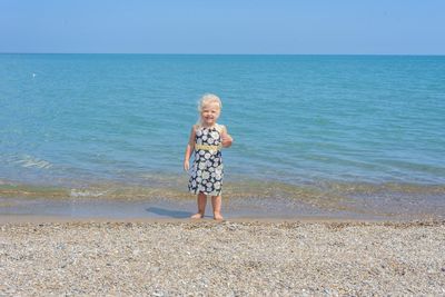 Portrait of cut girl standing on beach against clear sky