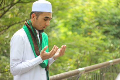 Mid adult man praying while standing by railing at park