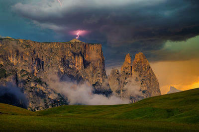 Huge rock formation of rosengarten / italy with lightning and dark clouds and sun glowing background