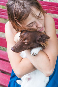 A girl in a blue sundress sits on a bench and hugs a little brown and white dog. love pets, dog day.