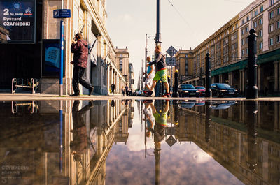 Reflection of people on canal by buildings in city