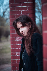 Portrait of young woman standing by brick wall