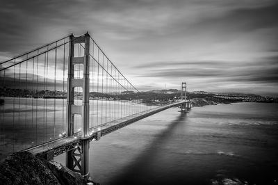 Suspension bridge over river against cloudy sky