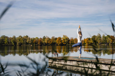 Woman practicing yoga in front of lake on sunny day