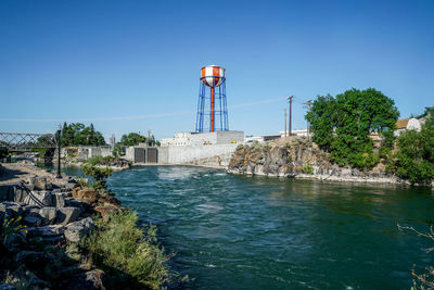 Water tower by sea against clear blue sky