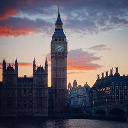 Big ben by thames river against sky during sunset