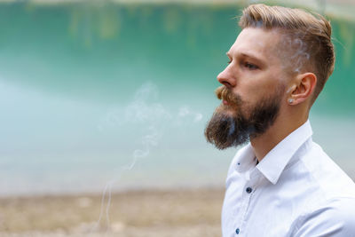 Business caucasian young bearded man in a white shirt smokes a cigarette