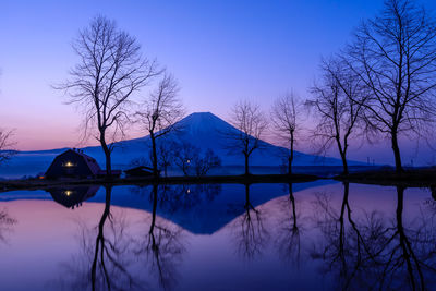 Bare trees by lake against sky during winter