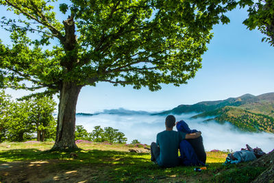 Rear view of couple sitting on mountain against sky