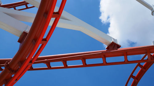 Twisted red roller coaster tracks with blue sky.