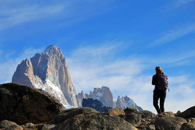 Rear view of woman standing on rock against sky