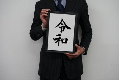 Midsection of man holding paper while standing against white background