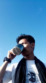 Low angle view of young man holding blue sky