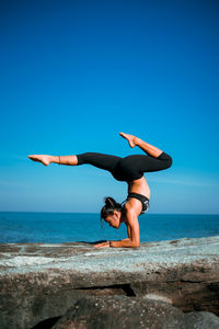 Woman jumping on beach against clear blue sky