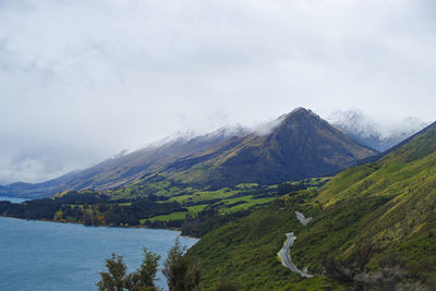 Scenic view of mountains by lake against cloudy sky