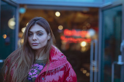 Portrait of young woman wearing warm clothing while standing against entrance at dusk