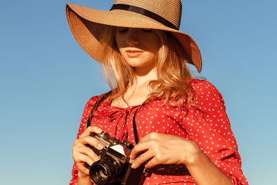 Young woman holding camera against blue background