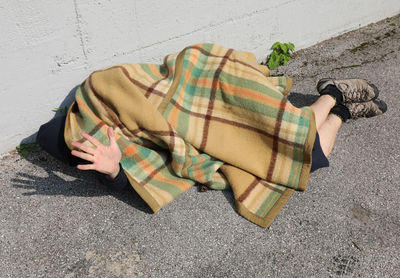 Young homeless man under an old blanket and his hand raised
