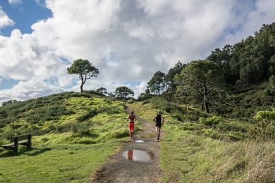 Rear view of friends jogging on field against cloudy sky