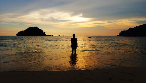 Silhouette man standing on beach against sky during sunset