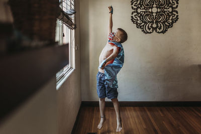 Young boy dressed as super hero with mask standing by window at home