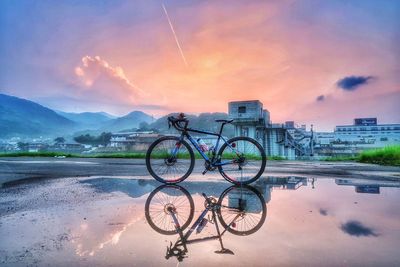 Bicycle by water against sky during sunset