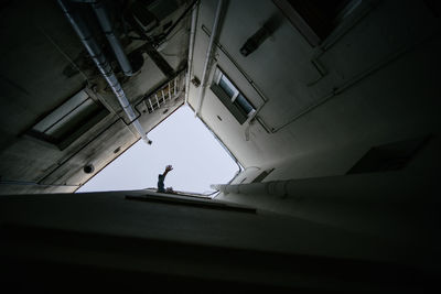 From below of anonymous person looking out of window of shabby building and waving hand