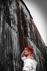 Low angle view of redhead woman standing by rusty corrugated wall