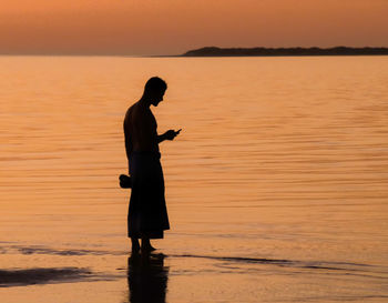 Side view of silhouette man standing at beach during sunset