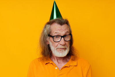 Portrait of senior man wearing party hat against yellow background