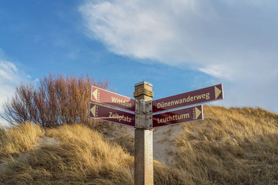 Road sign by bare tree against sky