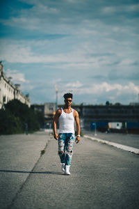 Portrait of handsome man walking on road against cloudy sky