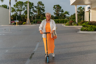 Portrait of happy elderly women riding push scooter in orang dress.