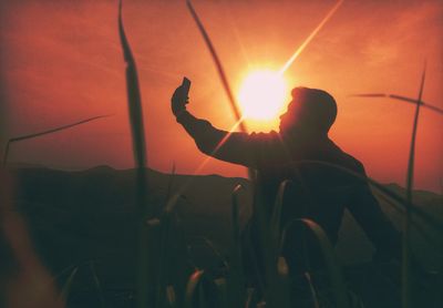 Silhouette man standing on field against orange sky