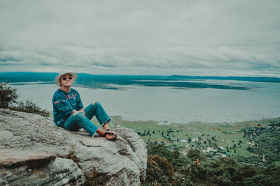 Man sitting on rock by sea against sky