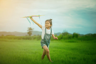 Full length of girl carrying kite on grass field