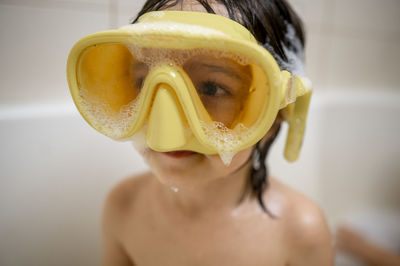 Cute boy wearing yellow swimming goggles with soap sud taking bath in bathroom