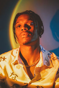 Serious african american male with braided hairstyle and chain looking at camera on dark background in studio with dim light