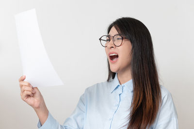 Portrait of young woman holding eyeglasses against white background