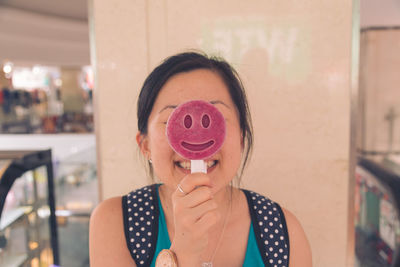 Happy young woman holding smiley face lollipop at restaurant