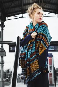 Young woman wearing scarf looking away while standing at railroad station platform