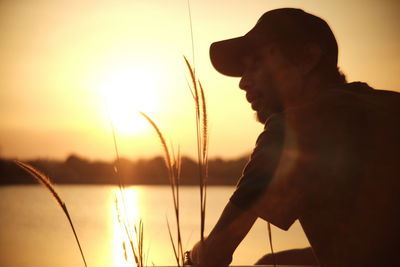 Man looking away while sitting by lake during sunset
