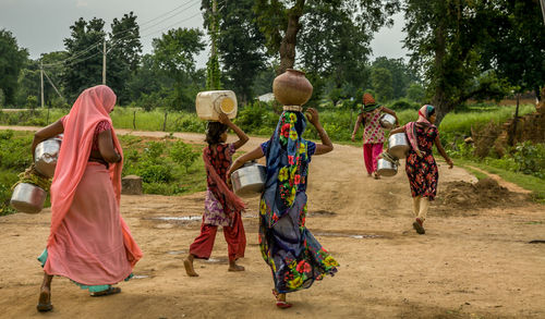 Rear view of woman carrying pitchers while walking on field